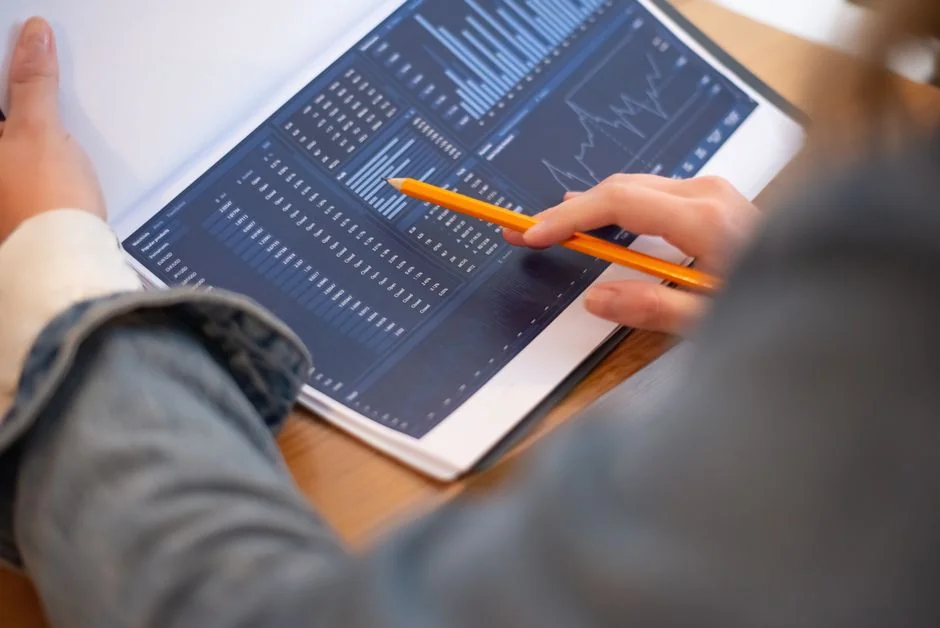 Hands using smartphone beside laptop with stock charts, showcasing digital trading.